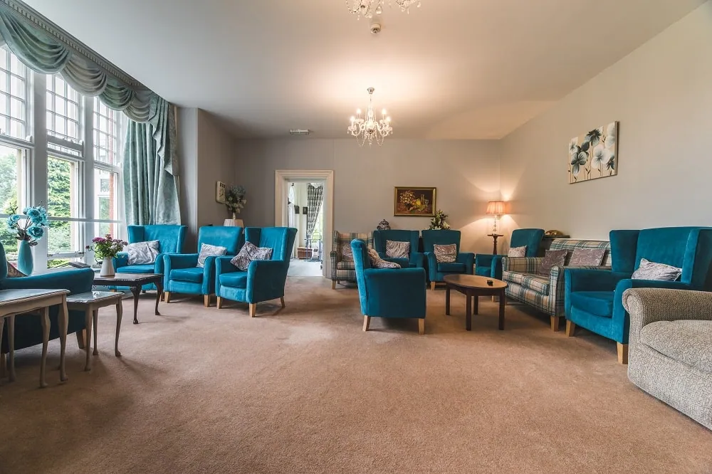 The residents' lounge with blue armchairs and sofas around coffee tables