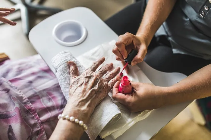A resident's hands being manicured with red nail polish