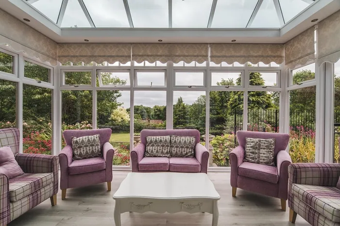 The orangery with purple sofas and armchairs under a glass roof, looking out to the garden